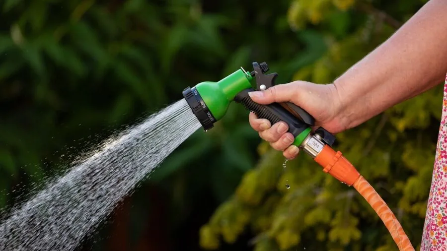 Person adjusting flexible hose nozzle to direct water mist spray in garden setting