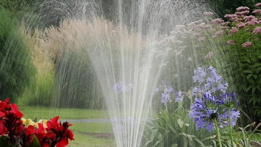 Person adjusting outdoor irrigation system in residential garden during morning watering routine
