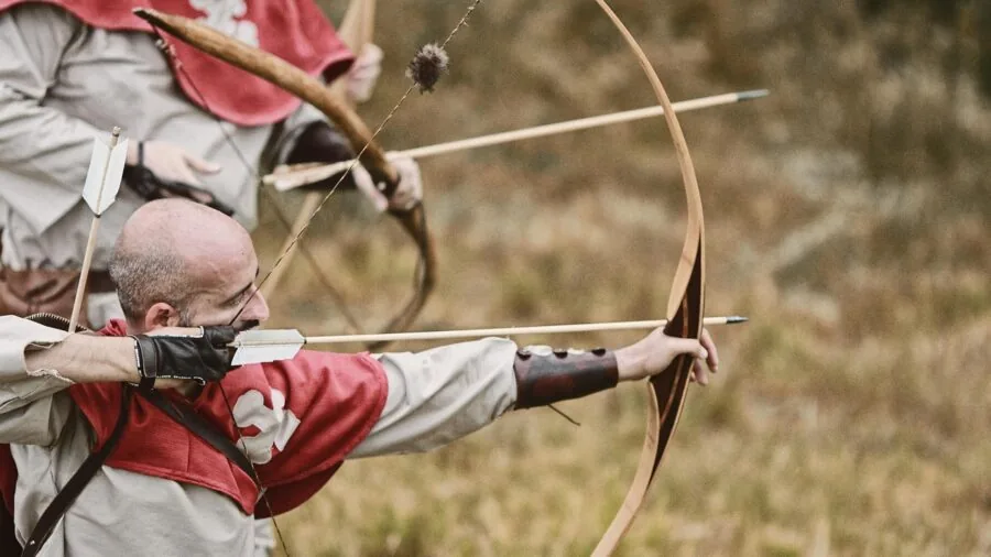 Person aiming crossbow at target in outdoor woodland setting, demonstrating proper stance and focus