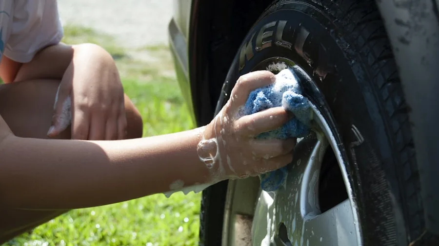 Person applying car polish by hand in outdoor driveway setting during daytime
