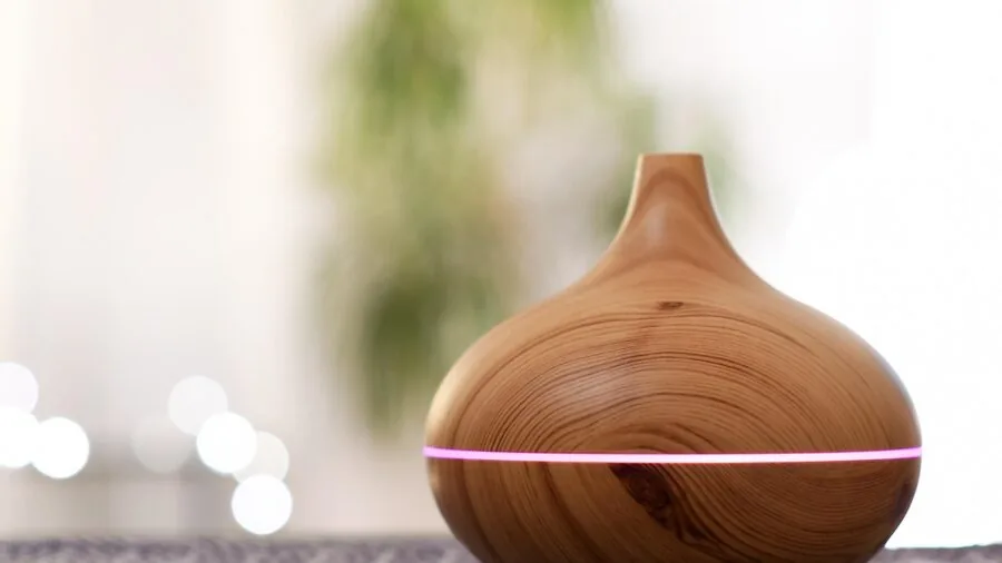 Person applying essential oil drops to a car diffuser while driving, with soft mist visible in natural light