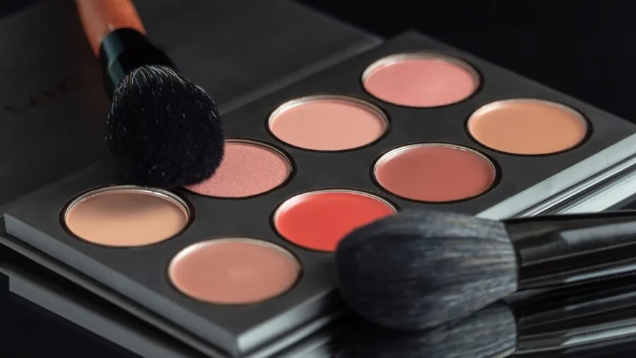 Person applying eyeshadow while looking in mirror, showing different skin tone representation