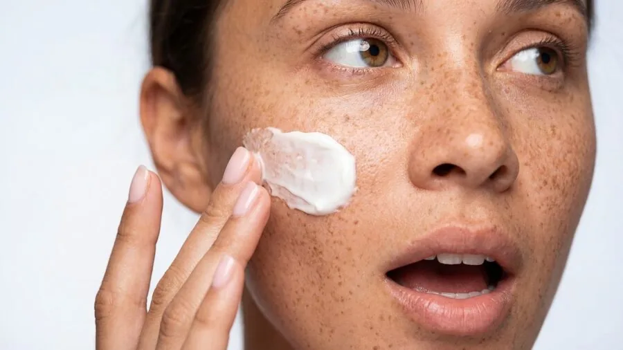 Person applying facial moisturizer with natural sunlight streaming through window