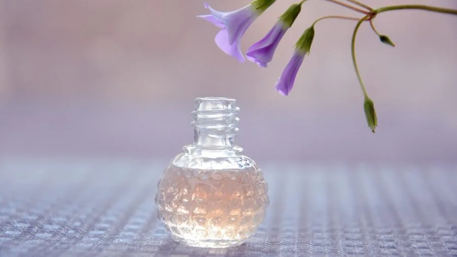 Person arranging and blending essential oils at a wooden table with natural lighting and botanical elements