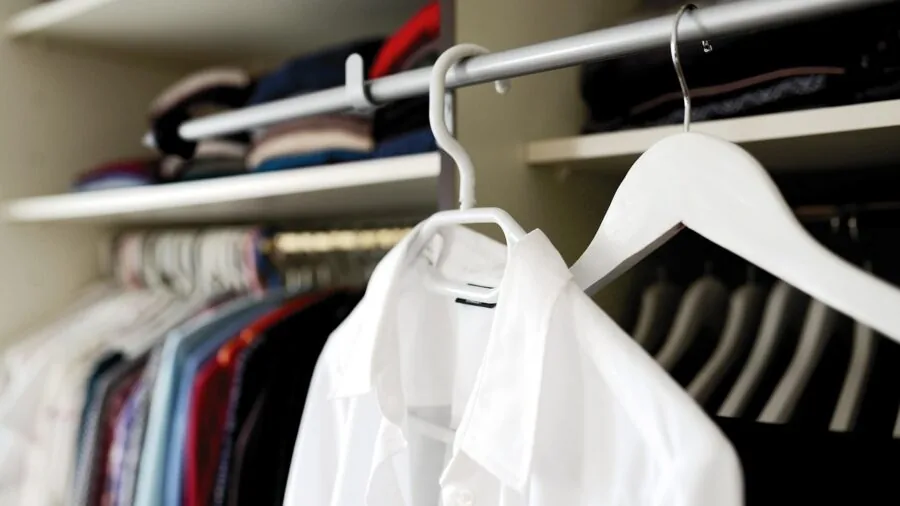 Person arranging clothing inside a wooden wardrobe in a bedroom setting