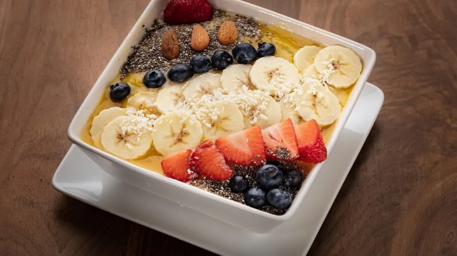 Person blending collagen powder into a nutritious smoothie bowl with fresh fruits and ingredients
