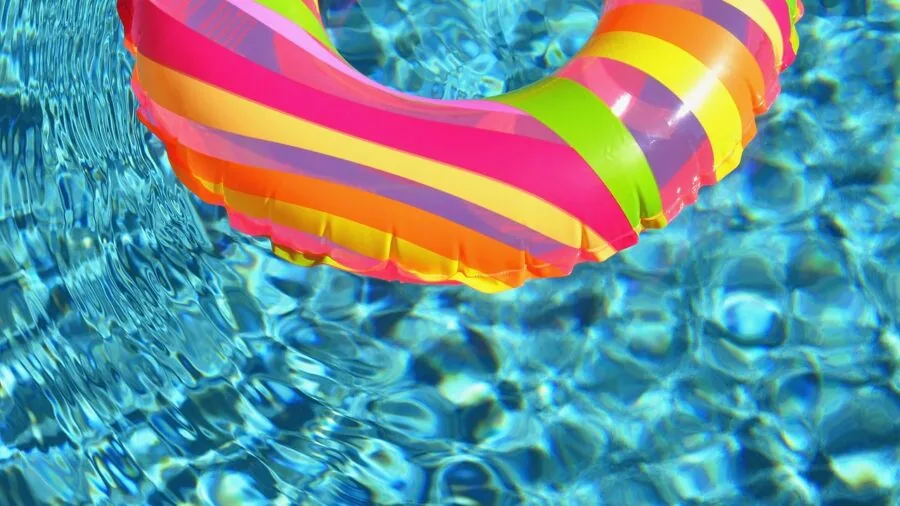 Person blowing up a colorful pool float by the swimming pool on a sunny day