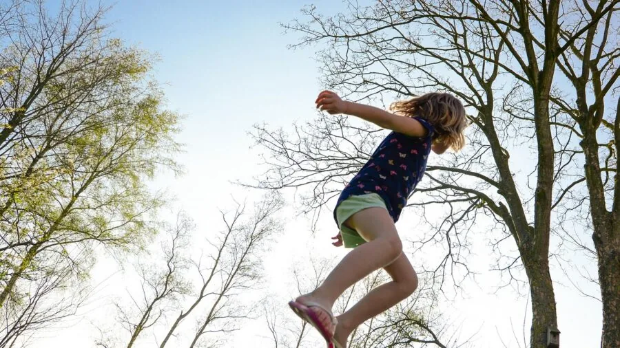 Person bouncing on trampoline in sunny backyard during outdoor fitness workout