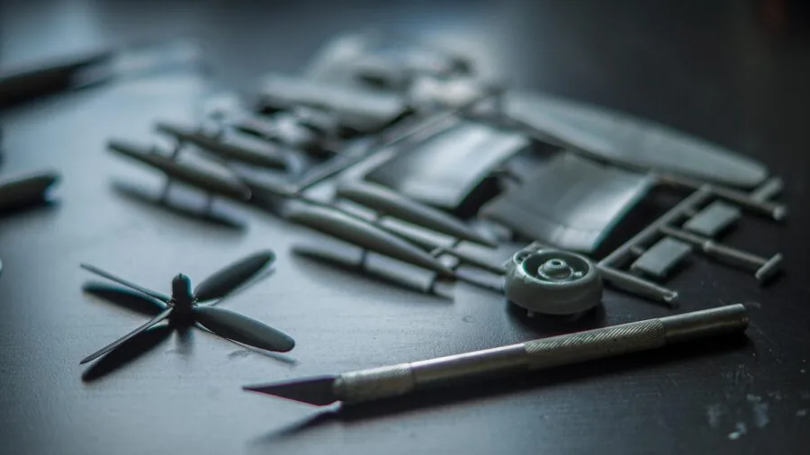 Person carefully assembling a detailed plastic scale model with precision tools and adhesive