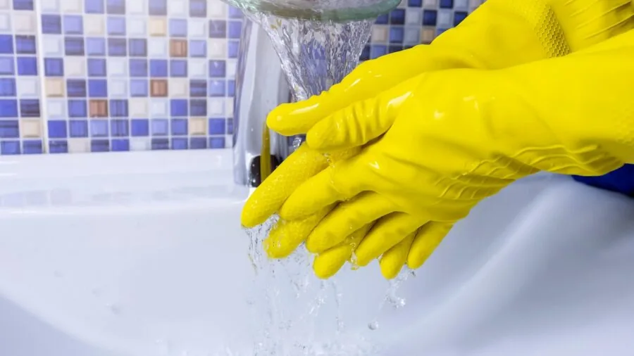 Person carefully hand washing a dark metal skillet under running water in a kitchen sink