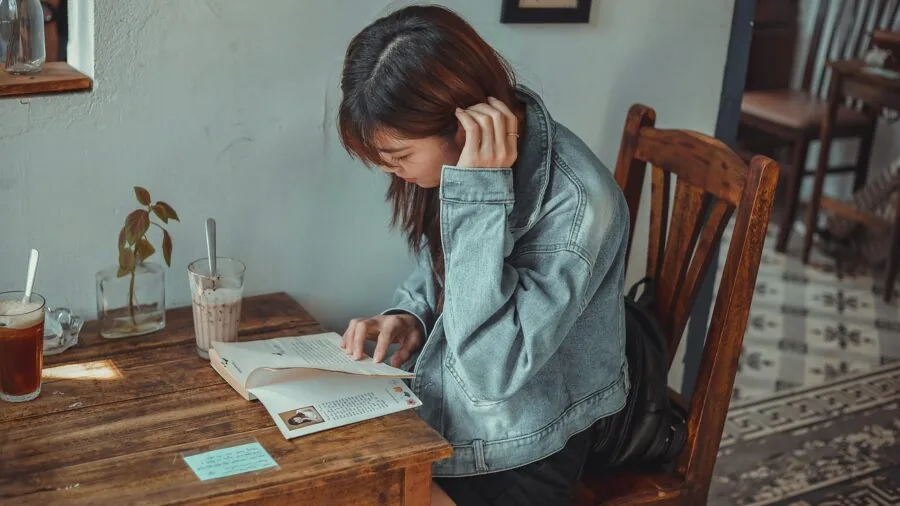 Person carefully reading instruction manual with diagrams at wooden table during daytime