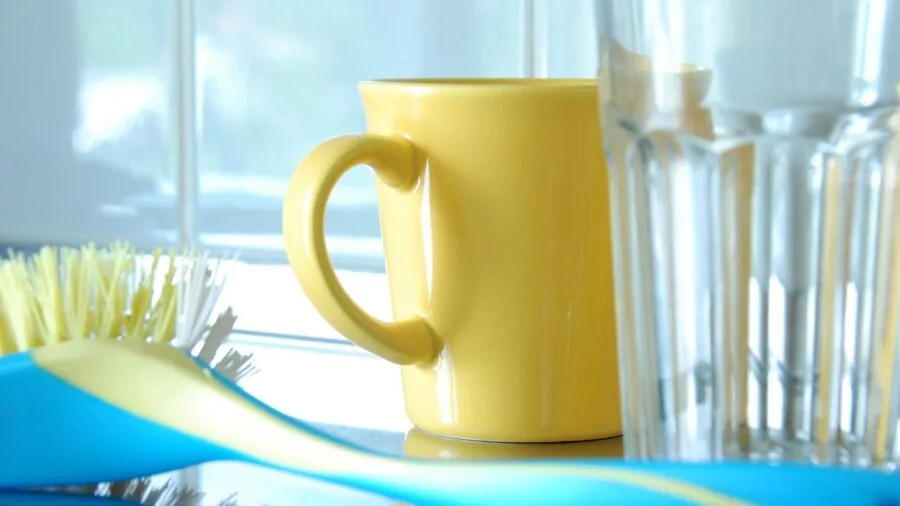 Person carefully washing dishes by hand in a home kitchen sink with warm water and soap
