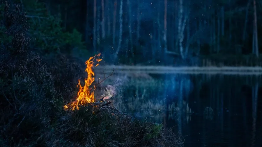 Person carrying compact fire pit equipment through outdoor campsite during camping trip