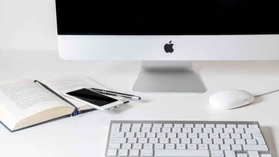 Person charging smartphone at desk with reading lamp in home office environment