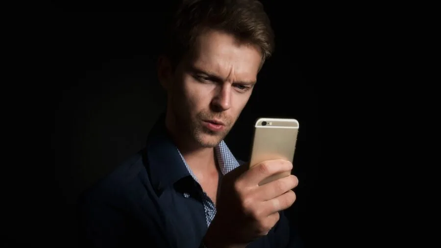 Person checking smartphone app while standing in residential garden with green lawn and plants