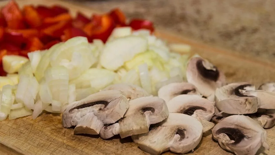 Person chopping fresh vegetables on wooden cutting board in bright kitchen