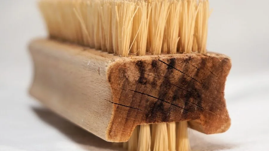 Person cleaning accumulated cat hair from grooming brush under running water in sink