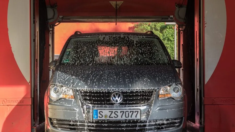 Person cleaning car wheel with soapy foam and cleaning supplies in natural daylight