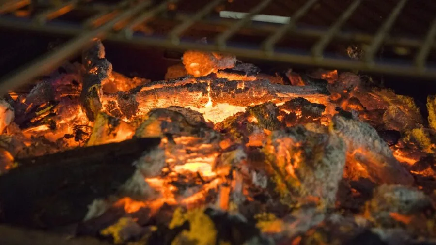 Person cleaning charcoal grill ash with brush and dustpan during backyard maintenance