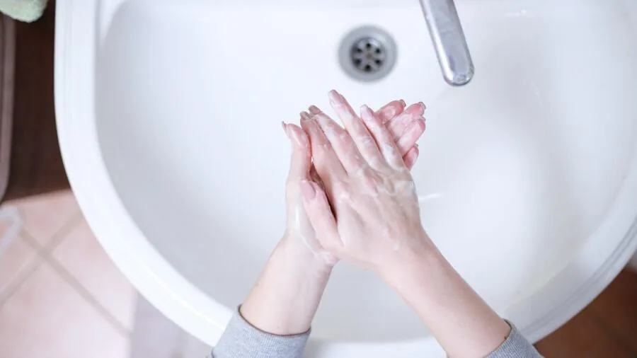 Person cleaning disassembled razor parts at bathroom sink during morning grooming routine