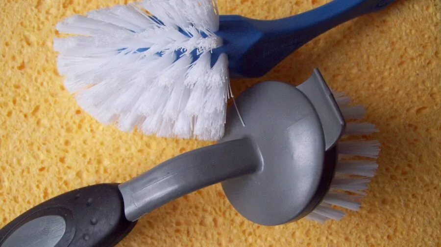 Person cleaning kitchen appliance with brush and soapy water in bright home kitchen
