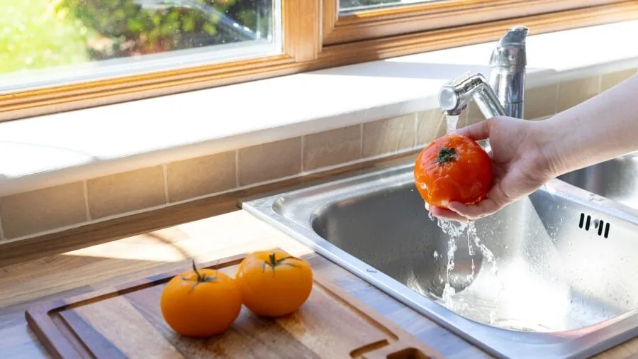 Person cleaning kitchen tools under running water in a modern sink with natural lighting