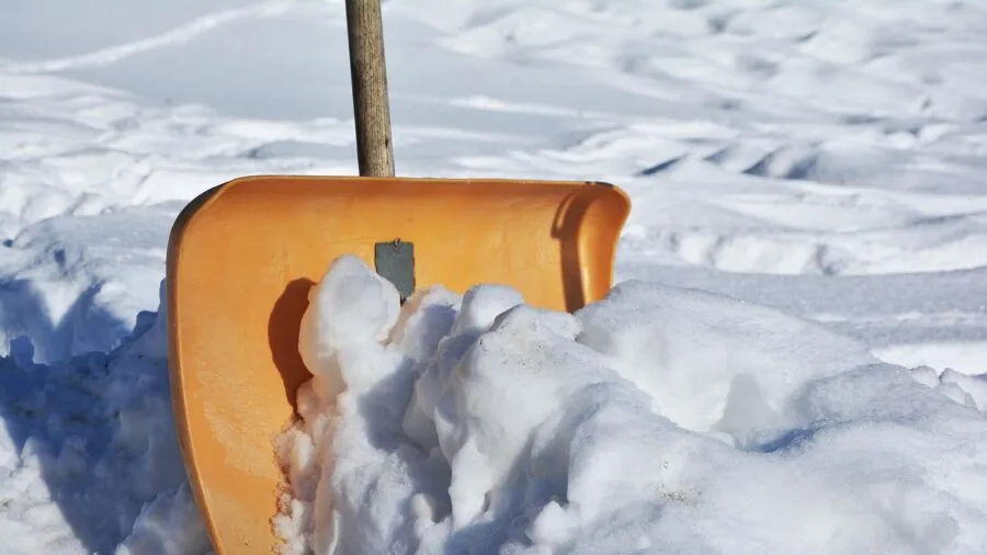 Person clearing snow from residential driveway during winter snowstorm with shovel