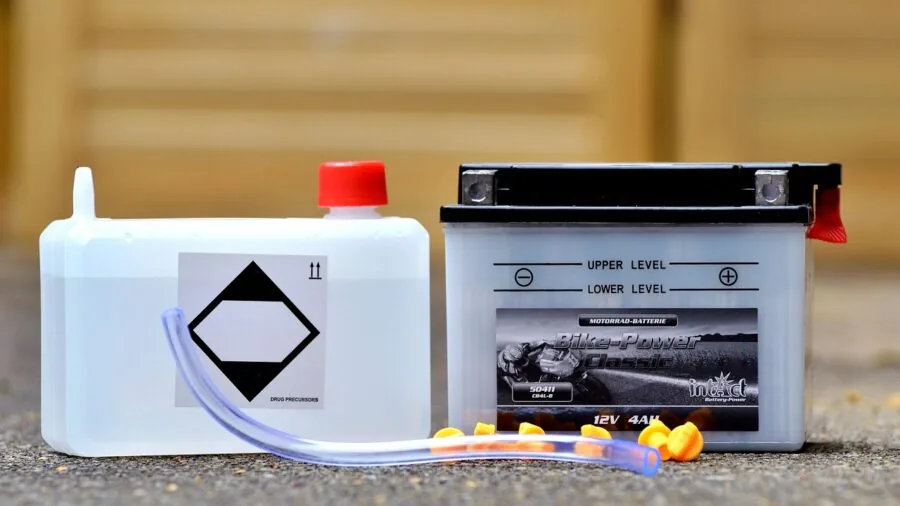 Person connecting battery charger cables to motorcycle battery in garage workshop setting