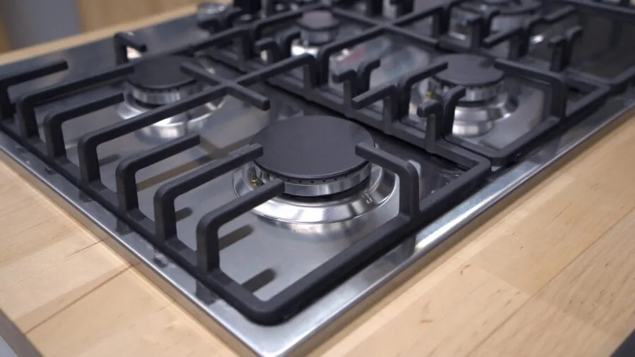 Person cooking with griddle pan on kitchen stovetop with multiple burners