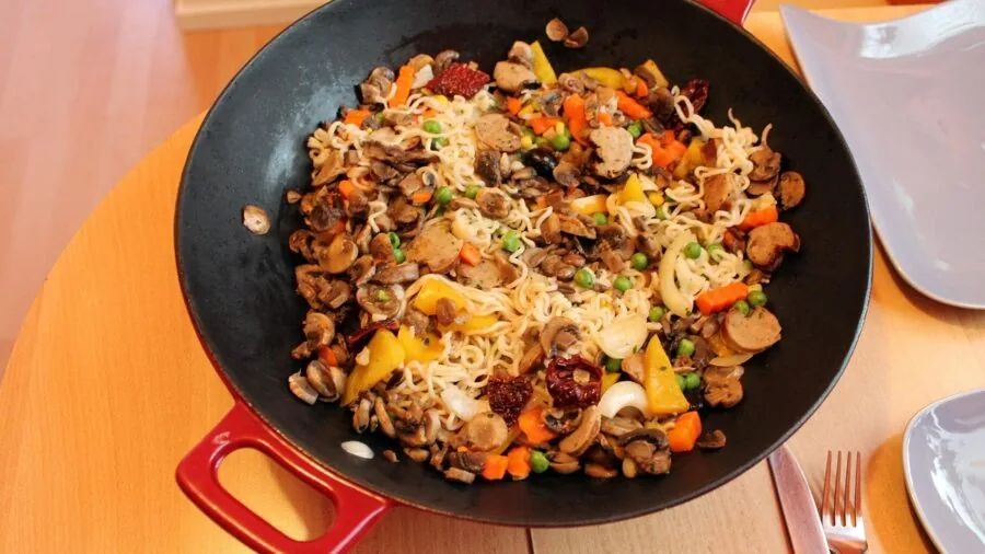 Person cooking with wok in home kitchen, stir-frying vegetables over heat