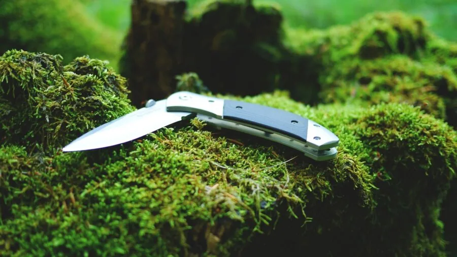 Person demonstrating knife skills during wilderness camping adventure in natural setting