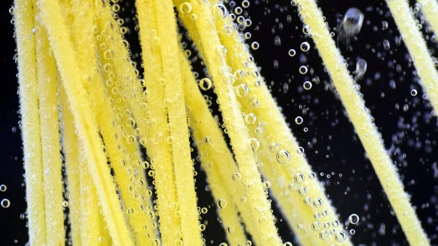 Person draining freshly cooked pasta in a kitchen sink during meal preparation