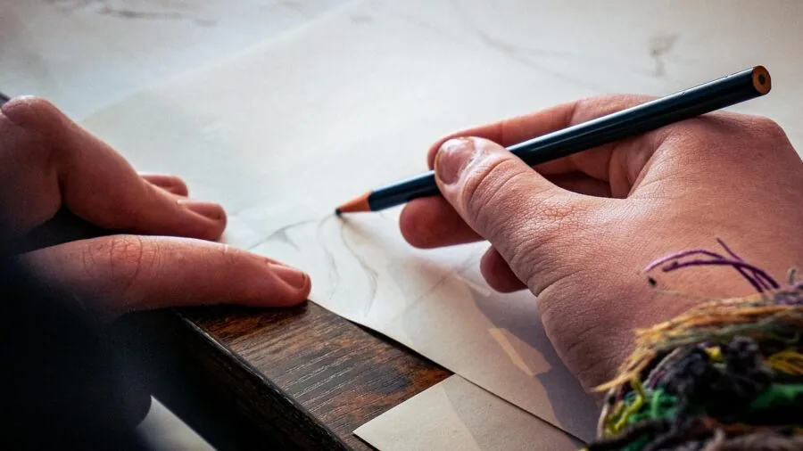 Person drawing in sketchbook at outdoor table with natural lighting