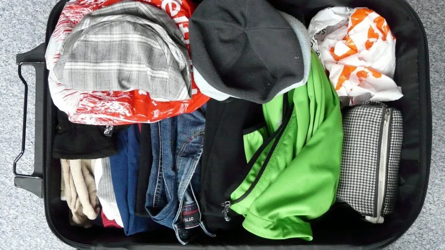 Person efficiently packing folded clothes into a suitcase for travel