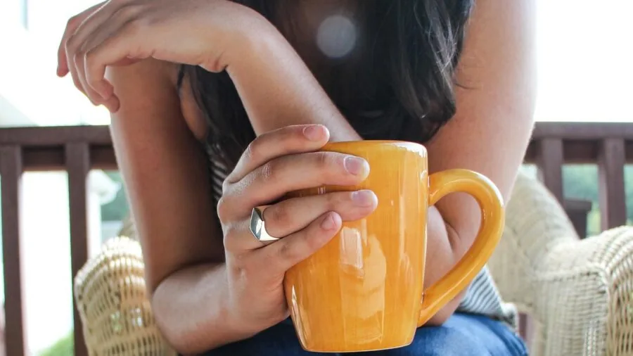 Person enjoying hot beverage from small mug while camping in wilderness setting