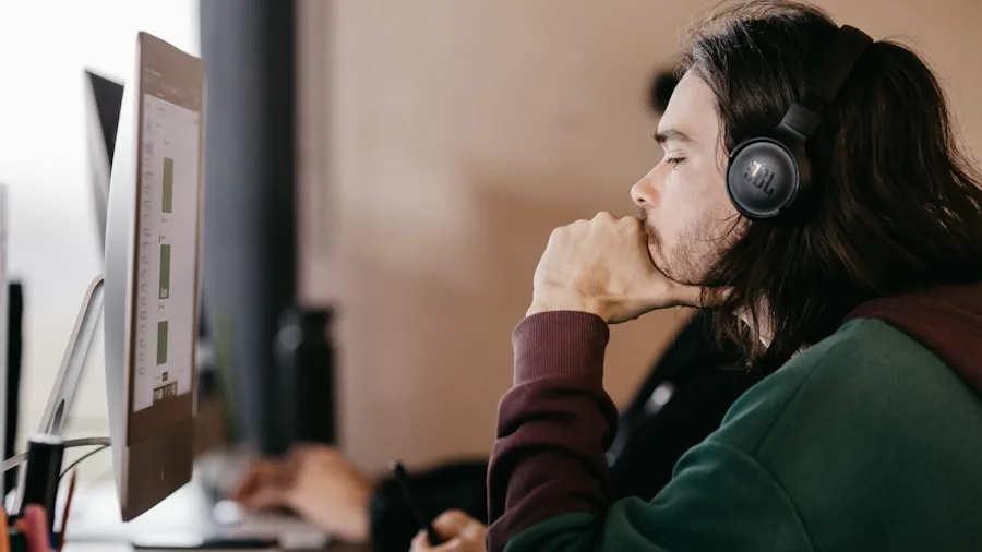 Person enjoying music with wired headphones while working on laptop and phone at desk