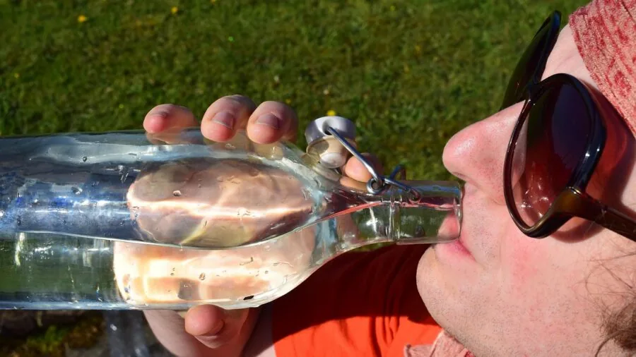 Person enjoying water from a bottle during outdoor activity, showing natural drinking posture and hydration habit