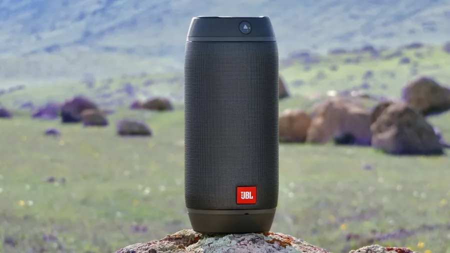 Person enjoying waterproof speaker by lake during outdoor adventure with natural landscape