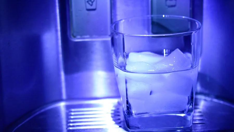 Person filling a glass with cold water dispensed from a refrigerator in a home kitchen
