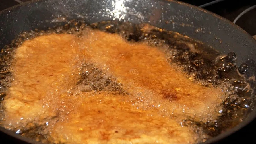 Person filtering cooking oil through fine mesh strainer into glass container in home kitchen