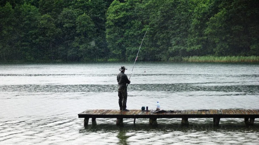 Person fishing from kayak on calm water with portable equipment