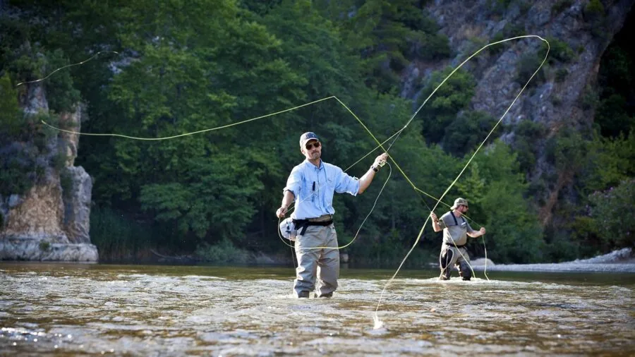 Person fishing in calm freshwater stream with rod and reel during outdoor adventure