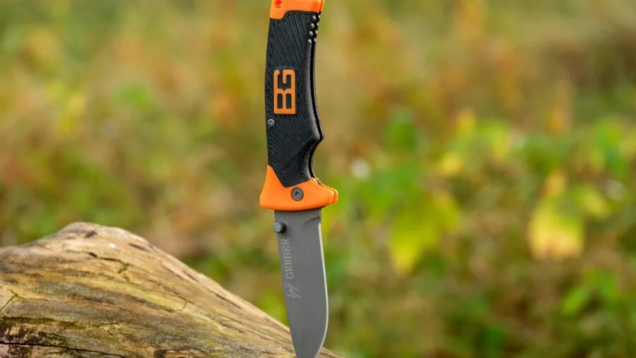 Person gripping a camping knife while chopping firewood at an outdoor campsite