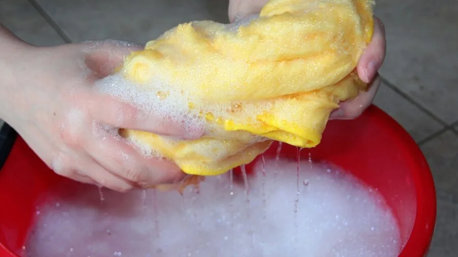 Person hand-washing a pet food bowl in kitchen sink with water and soap