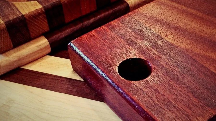 Person hand washing a wooden cutting board under running water in a kitchen sink