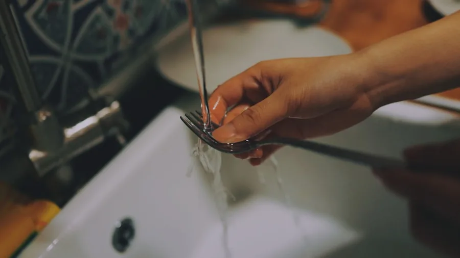Person hand washing kitchen knives under running water at sink for proper maintenance and care