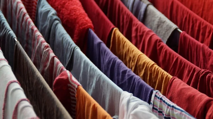 Person hanging delicate clothes on a wooden drying rack in a small apartment bedroom