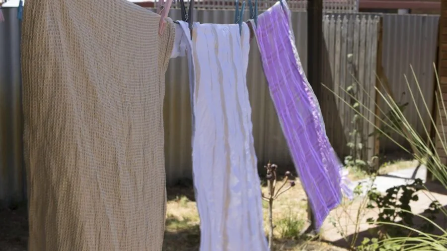 Person hanging wet yoga towel to air dry on clothesline in bright natural light