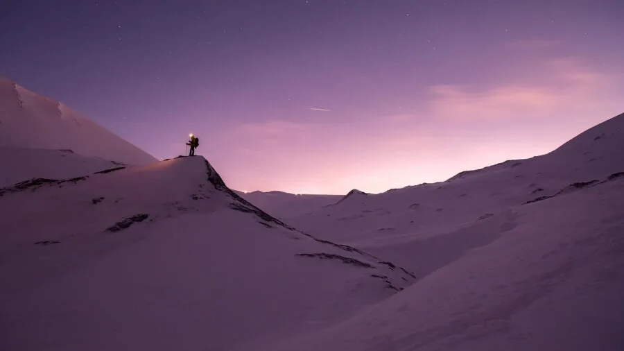 Person hiking on snow-covered mountain trail with ice and winter landscape