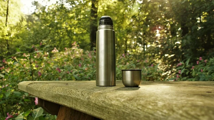 Person hiking on trail holding insulated mug while walking through forest